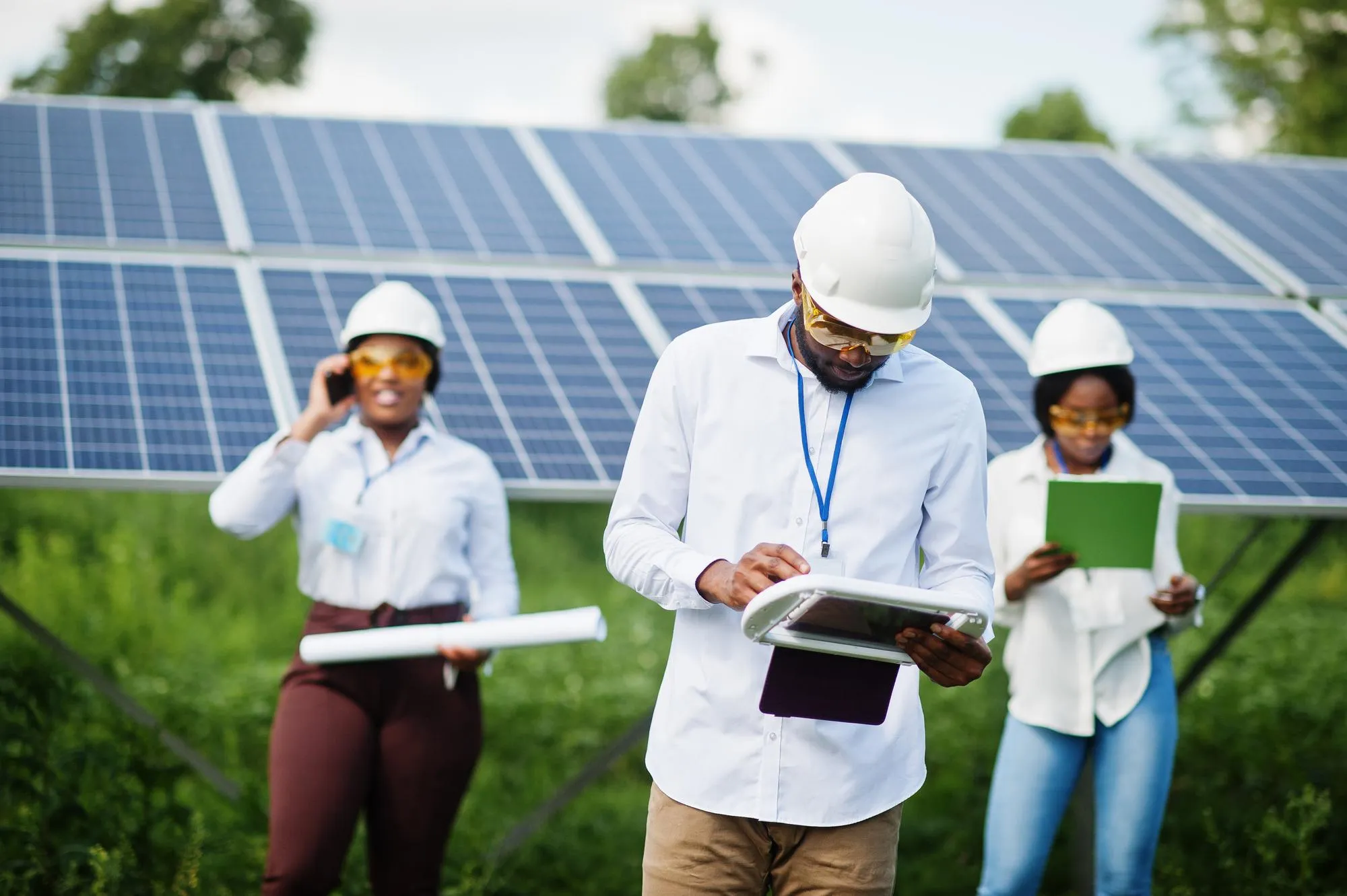 Equipo de ingenieros con cascos y gafas de seguridad trabajando con paneles solares al aire libre.